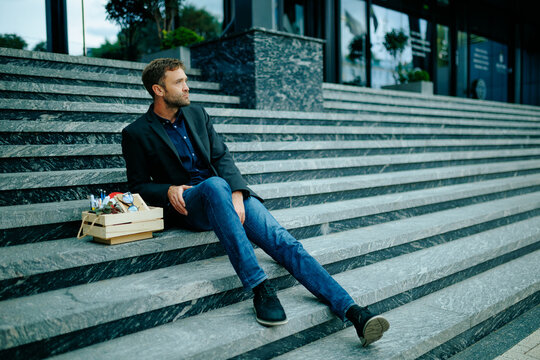 Fired job defeat leaves exhausted corporate professional sitting on outdoor concrete steps.