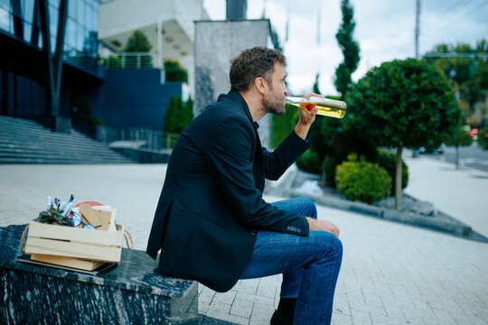 Recession crisis forces desperate professional to drink alcohol on outdoor stairs in sorrow.