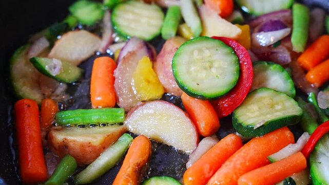 Colorful vegetable medley glistening with oil in close up, baby carrots, zucchini rounds, red pepper, green beans, potatoes and onion filling the whole view, concept of healthy eating and vibrant pla