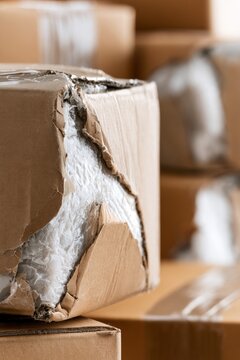 Damaged cardboard box among stacked packages in a warehouse setting