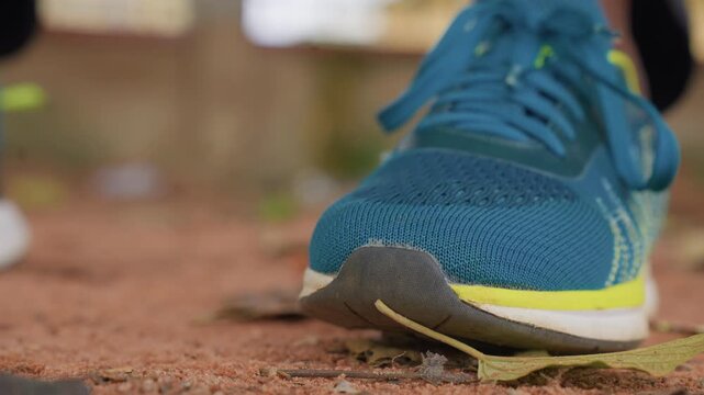 Close up sequence shows one foot wearing blue running shoe with yellow accents stepping over rough ground focusing on sole and laces. scene emphasizes movement through various angles