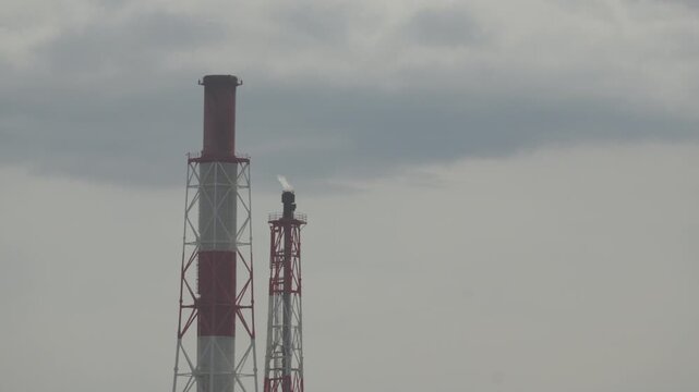 Low angle view of tall red and white factory chimneys reaching into cloudy sky in Tomakomai, Hokkaido, Japan. Fixed 4K video.
