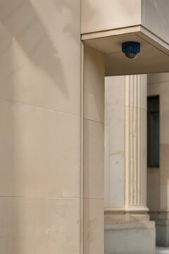 Dome security camera mounted on civic building exterior. Outdoor video surveillance dome beneath stone cornice with fluted column in background. Vertical composition