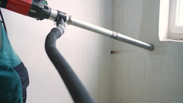 Construction worker using industrial core drill to make hole in concrete wall with dust extractor