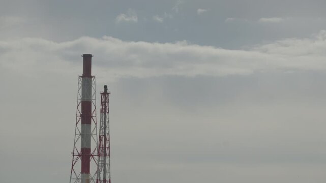 Low angle view of tall red and white factory chimneys reaching into cloudy sky in Tomakomai, Hokkaido, Japan. Fixed 4K video.