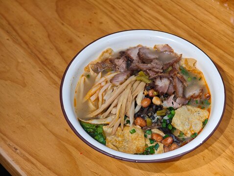 a bowl of Liuzhou Luosifen river snail rice noodles with toppings on a wooden table