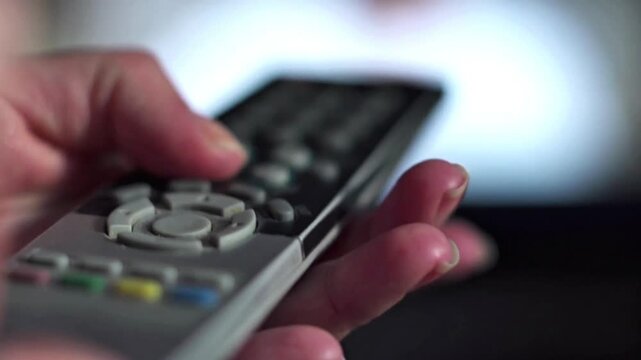 Close-up of a Person's Hand Holding a TV Remote Control in Front of a Blurred Screen, Home Entertainment and Media Leisure Concept