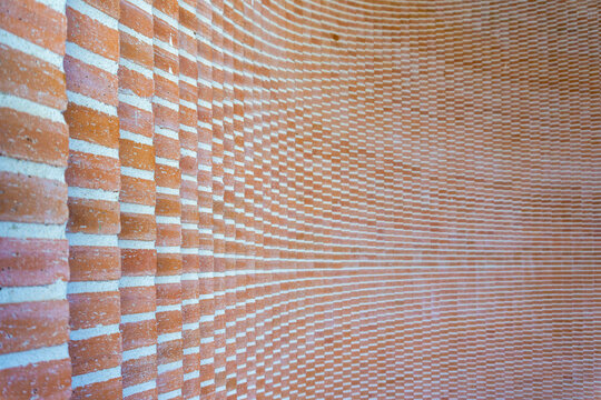 Orange brick wall featuring a distinctive curved architecture, forming a dynamic abstract pattern with horizontal lines and varying depths, providing a textured background