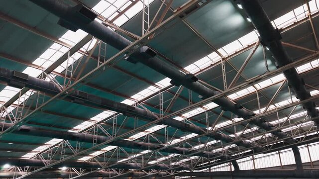 Industrial warehouse roof structure with steel trusses, ventilation ducts and skylights, low angle view