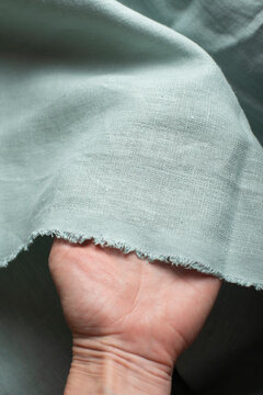 Close-up photograph of a hand holding a soft piece of mint green natural linen fabric
