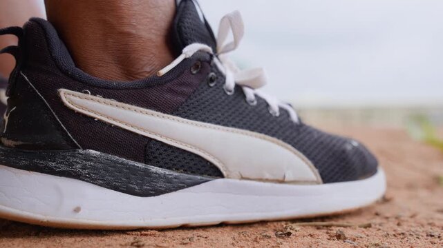 Close up shows detailed textures from sand stuck to old running shoe. focus remains steady throughout highlighting fabric weave patterns and scuffed sole against blurred sandy background