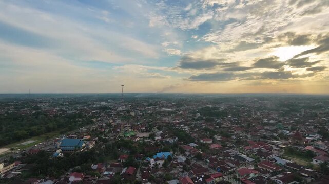 Aerial view of a small town settlement during sunset, with houses and buildings under a dramatic cloudy sky. Urban landscape, evening twilight, and community travel concept.