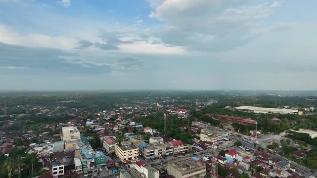Aerial view of a quiet small town settlement with dense red-roofed houses, narrow streets, and lush green tropical nature surrounding the urban area under a bright daylight sky.