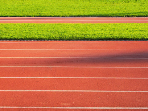 Red running track lanes with white lines next to green grass athletic field