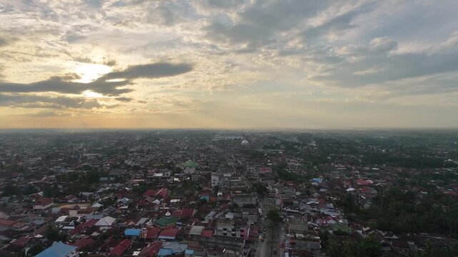 Aerial view of a densely populated town with countless red-roofed houses and buildings stretching to the horizon under a dramatic cloudy sunset sky. Urban landscape and evening atmosphere