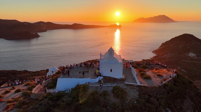 drone orbiting shot of a sunset on Greek island of Milos with a traditional whitewashed Greek church on the hilltop, cinematic drone video of vacation in Greece, holiday in the Cyclades
