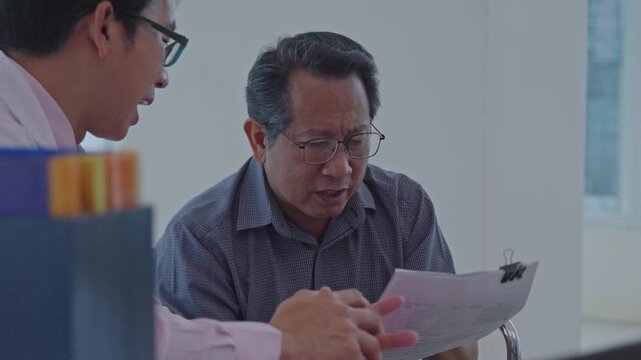 Asian senior man business meeting office, discussion with colleague reviewing document, gesture during conversation, expressing concern while explaining idea and collaborative review of business