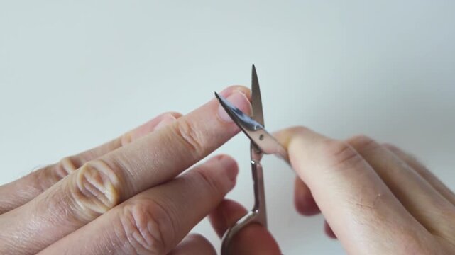 Hands trimming a fingernail with manicure scissors