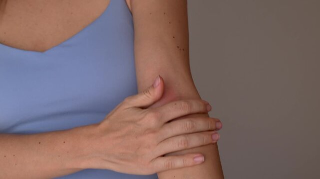 Young woman shows red rash on inner elbow on gray background, demonstrating skin allergy, irritation, dermatitis and eczema flare