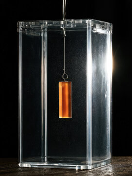 Amber pheromone lure suspended inside clear plastic pest trap with dramatic backlight, creating precise biological monitoring scene