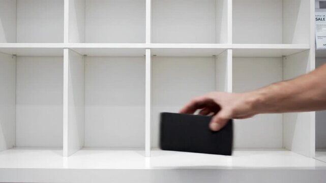 Nearly empty electronics store display. Man removing black box from white shelf. Retail inventory and stock clearance concept