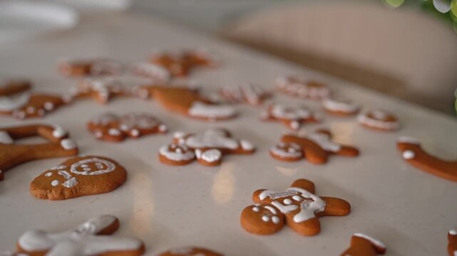Iced gingerbread cookies cooling on table with blurred Christmas tree lights. Warm holiday glow, cozy indoor kitchen dining scene.