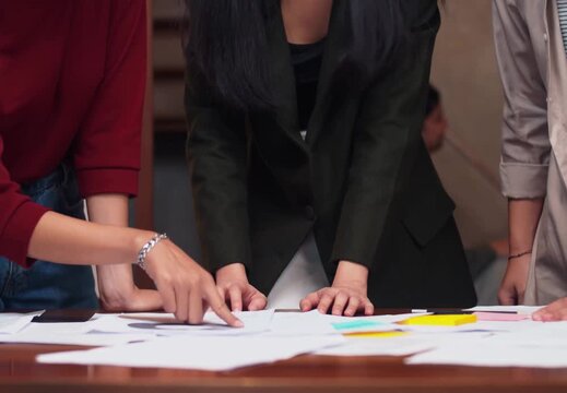 Colleagues at a workbench desk making brush corrections on printed sheets with markers and pens.
