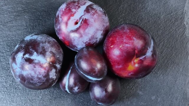 Plums different varieties and sizes on black flat slate plate