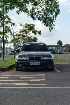 Dark grey BMW 3 Series E46 sports sedan front view parked in asphalt parking lot under green trees