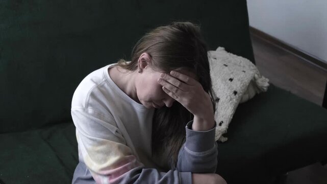 A young woman or woman is crying or suffering from depression, sitting on the sofa and covering her face with her hand.