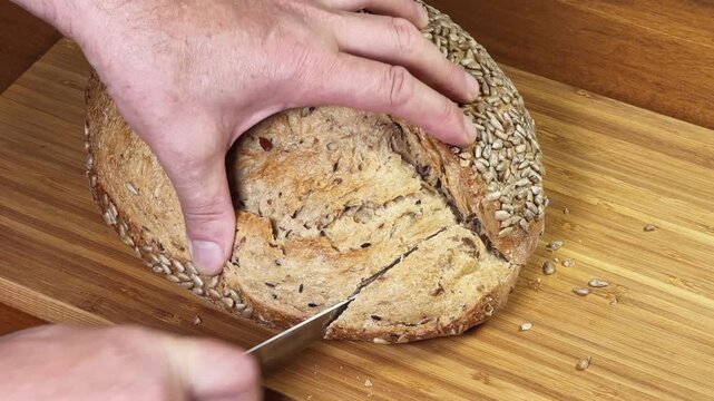 Slicing artisan bread sprinkled with sunflower seeds with serrated knife