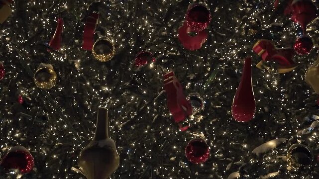 Sparkling Christmas tree adorned with red and gold ornaments and thousands of tiny white lights at night. Slow pan over festive holiday decorations