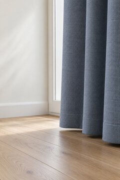 Blue-gray curtain hem beside a white window and wood floor