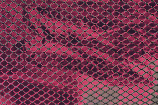Abstract background of dark pink metal diamond mesh grid pattern over reflective metallic foil surface.