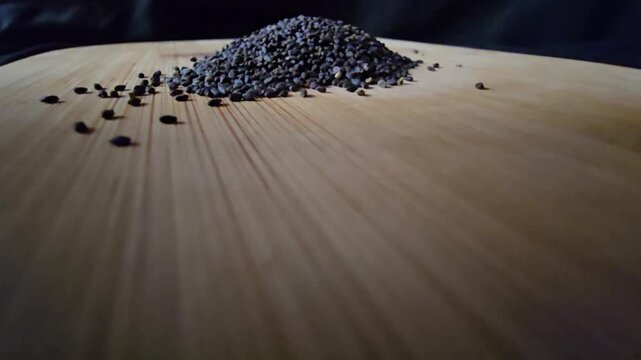 Low-angle wide macro video of a neat pile of organic black basil seeds on a textured wooden board. Ideal for health food, cooking, and natural wellness concepts.   