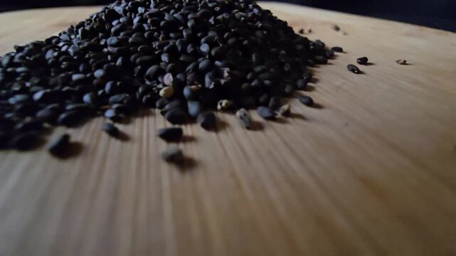Macro video of a neat pile of organic black basil seeds on a textured wooden board, captured with a close-up angle. Perfect for health food, cooking, and natural wellness projects.   