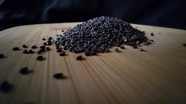 Macro video of a neat pile of organic black basil seeds on a textured wooden board, with a dark background. Ideal for health food, cooking, and natural wellness concepts.   
