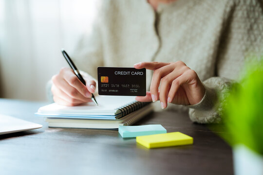 A close-up shot of a woman managing her personal finances using a credit card, a notebook, a smartphone, and a laptop.