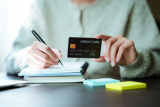 A close-up shot of a woman managing her personal finances using a credit card, a notebook, a smartphone, and a laptop.