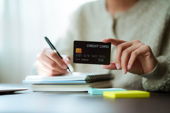 A close-up shot of a woman managing her personal finances using a credit card, a notebook, a smartphone, and a laptop.