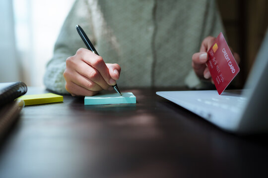 A close-up shot of a woman managing her personal finances using a credit card, a notebook, a smartphone, and a laptop.