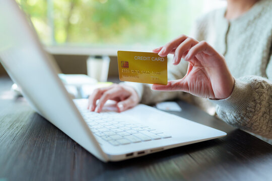 A close-up shot of a woman managing her personal finances using a credit card, a notebook, a smartphone, and a laptop.