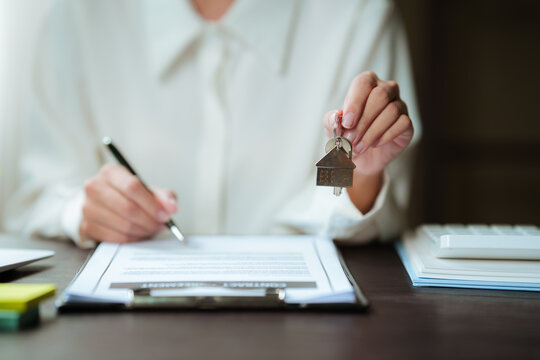 Real estate agent signing a property contract while holding house keys, representing home purchase, property transactions, and real estate services.