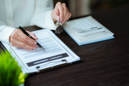 Real estate agent signing a property contract while holding house keys, representing home purchase, property transactions, and real estate services.