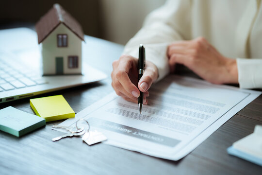 Real estate professional signing a property contract beside a house model and keys, representing home purchase, property transactions, and real estate investment.