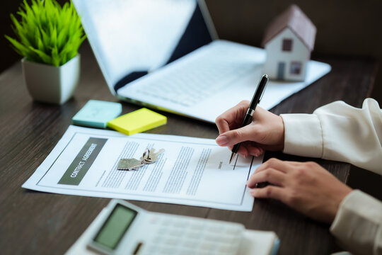 Real estate professional signing a property contract beside a house model and keys, representing home purchase, property transactions, and real estate investment.