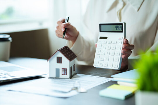 Real estate professional calculating property costs with a calculator, house model, and documents, representing home finance, mortgage planning, and property investment.