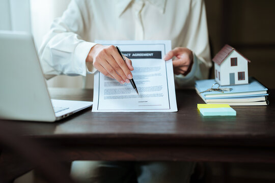 Real estate professional working on a laptop beside a house model, property contract, and keys, representing home buying and real estate transactions.
