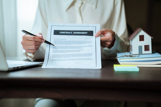 Real estate professional working on a laptop beside a house model, property contract, and keys, representing home buying and real estate transactions.
