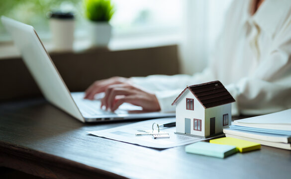 Real estate professional working on a laptop beside a house model, property contract, and keys, representing home buying and real estate transactions.